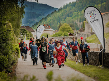 Gruppe läuft verkleidet und sportlich beim Caritas-Charity-Lauf mit Fahnen in bergiger Landschaft