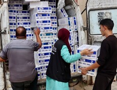 Mehrere Helfer*innen der Caritas Jerusalem laden Kisten mit Babynahrung aus einem Transporter. Der Wagen ist mit Hilfspaketen voll beladen.