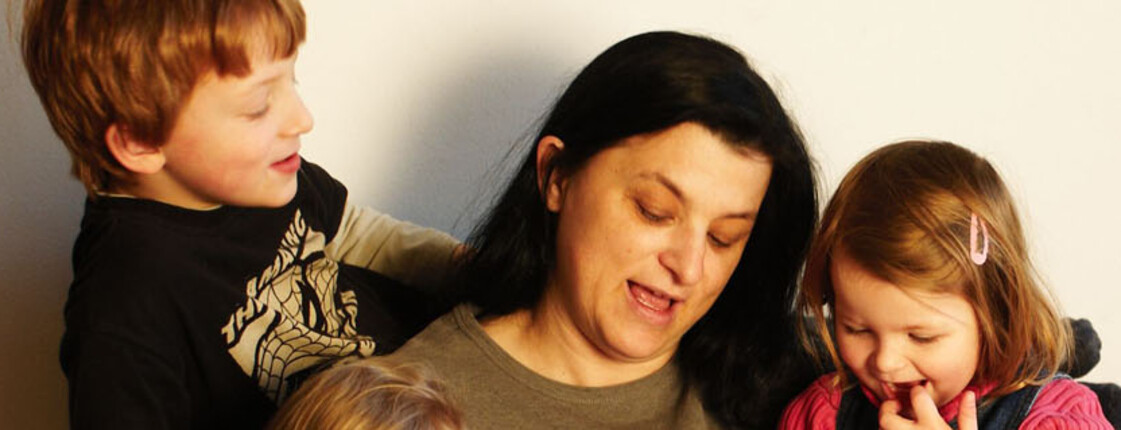Familien & Kinder – Unterstützung und Zusammenhalt  Eine Frau sitzt mit zwei Kindern zusammen und lächelt, alle wirken vertraut und fröhlich.
