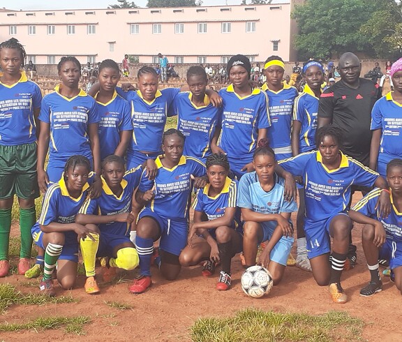 Ein Mädchenfußballteam in blauen Trikots posiert gemeinsam mit Trainern für ein Gruppenfoto.