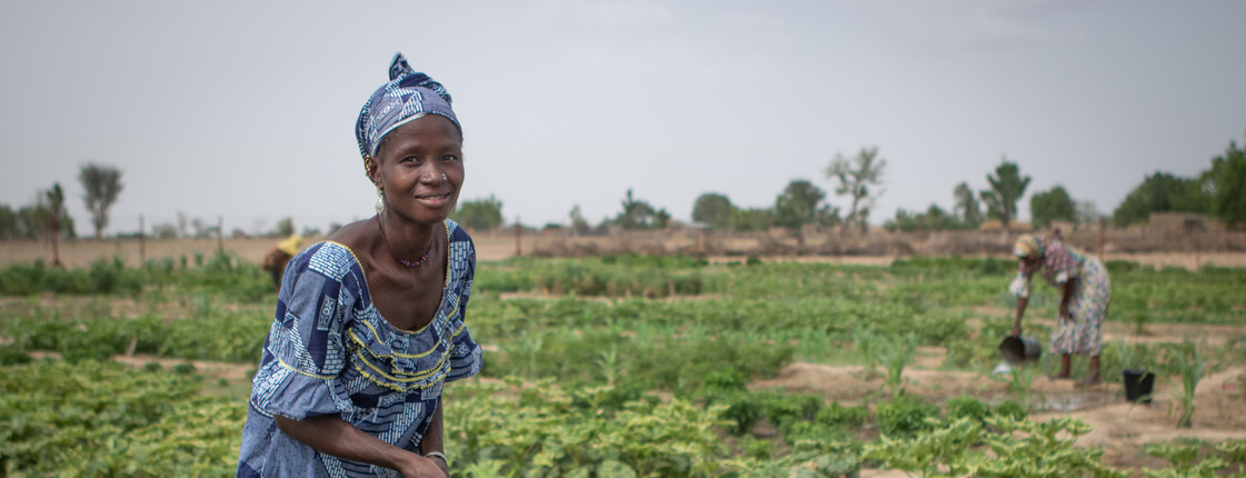 Auf einem Gemüsefeld in Burkina Faso schöpft eine Frau Wasser mit einem grünen Plastikeimer aus einem Bewässerungsbrunnen.