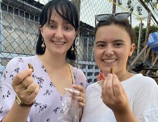 Zwei junge Erwachsene halten regionale Snacks in der Hand und lächeln in die Kamera.