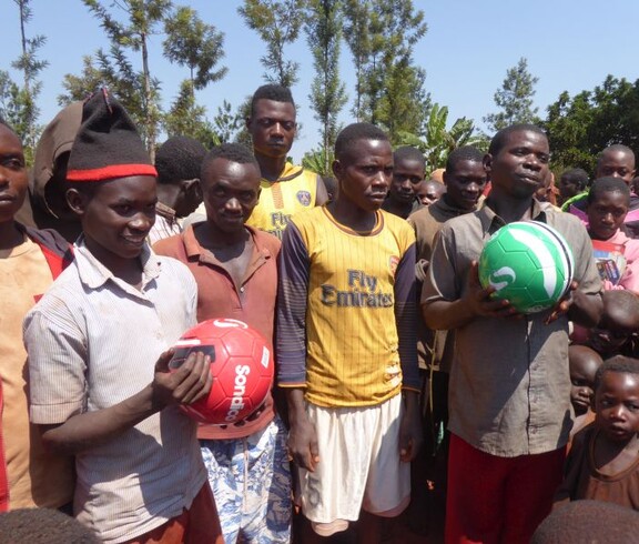 Eine Gruppe junger Burunder blickt in die Kamera. Zwei Burschen halten Fußbälle in der Hand. 