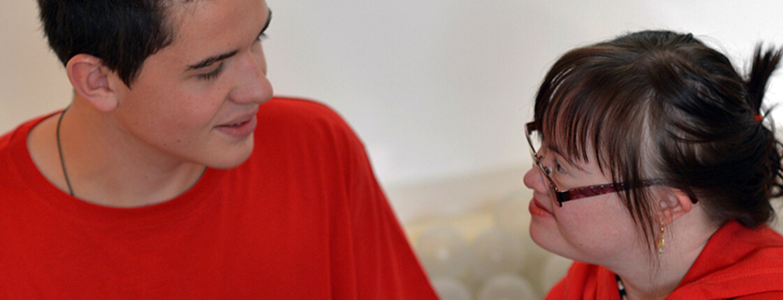 Ein junger Mann und eine junge Frau mit Behinderung lächeln einander an und unterhalten sich.