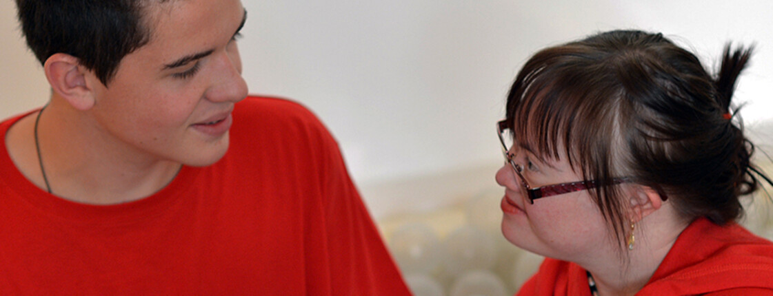 Ein junger Mann und eine junge Frau mit Behinderung lächeln einander an und unterhalten sich.