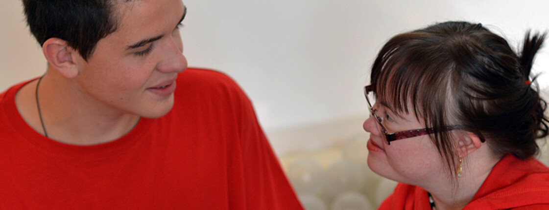 Ein junger Mann und eine junge Frau mit Behinderung lächeln einander an und unterhalten sich.