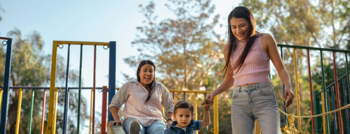 Zwei Frauen spielen mit einem Kind auf einem Spielplatz.