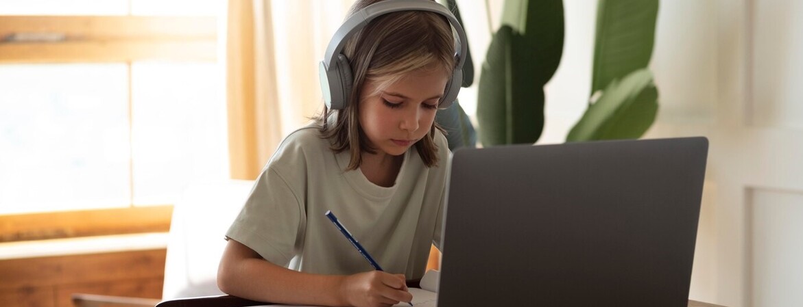 Onlinenachhilfe Kind mit Kopfhörer sitzt mit Heft vor einem Laptop