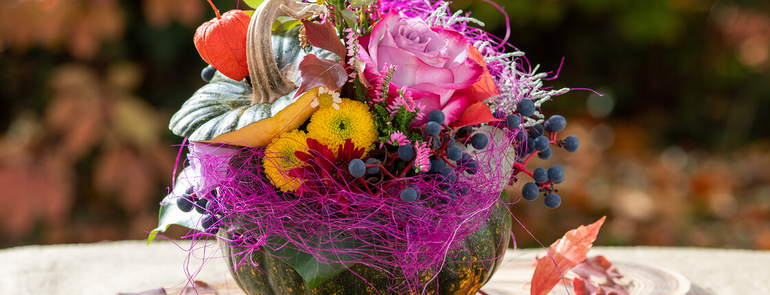 Herbstliches Arrangement aus Kürbis, Blumen und Beeren auf einem Tisch.