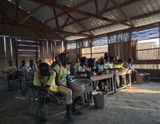 eine Gruppe junger Südsudanesen sitzt in einem düsteren Klassenzimmer und isst. 