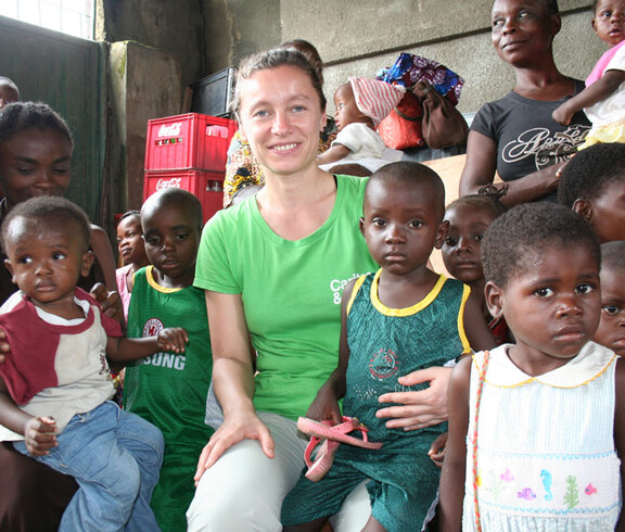 Andrea Fellner sitzt inmitten einer Gruppe von Kindern in der Ernährungsstation in N’sele und lächelt in die Kamera