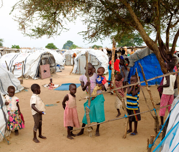 Gruppe von Kleinkindern und Kindern spielt zwischen provisorischen Zelten und Planen im Vertriebenenlager Gumbo, Südsudan.