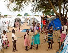 Gruppe von Kleinkindern und Kindern spielt zwischen provisorischen Zelten und Planen im Vertriebenenlager Gumbo, Südsudan.