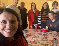 Mehrere Erwachsene und ein junger Mann sitzen und stehen um einen Tisch mit einer Geburtstags­torte.