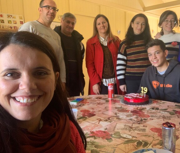 Mehrere Erwachsene und ein junger Mann sitzen und stehen um einen Tisch mit einer Geburtstags­torte.