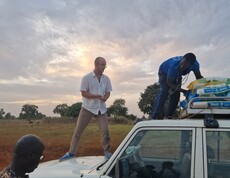 Mehrere Personen stehen auf und neben einem Geländewagen und entladen Säcke vom Dachträger.
