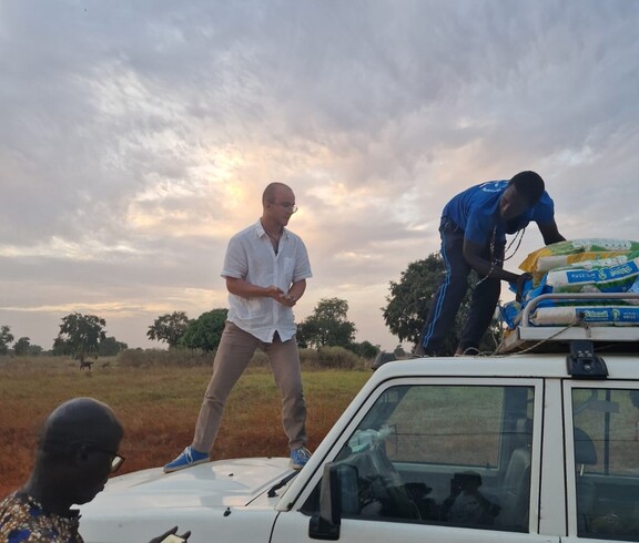 Mehrere Personen stehen auf und neben einem Geländewagen und entladen Säcke vom Dachträger.