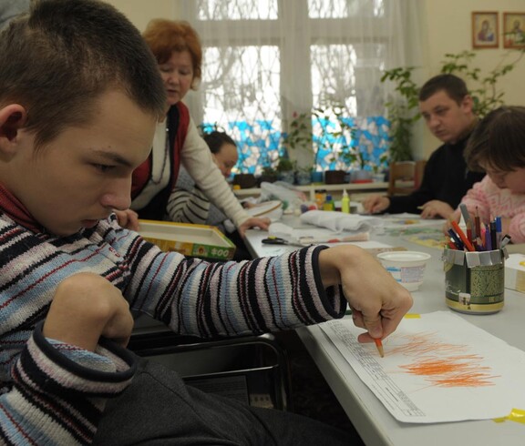 Junger Mensch mit Behinderung zeichnet an einem Tisch in einer betreuten Umgebung