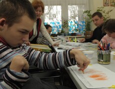 Junger Mensch mit Behinderung zeichnet an einem Tisch in einer betreuten Umgebung