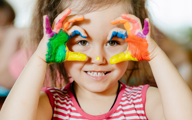 Mädchen im Kindergarten-Alter spielt mit bunten Bausteinen und lächelt durch Spielgerät