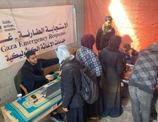 Frauen stehen an einem Tisch zur Erfassung durch Mitarbeitende vor Banner mit arabischer Aufschrift.