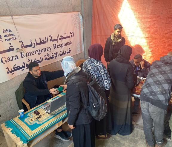 Frauen stehen an einem Tisch zur Erfassung durch Mitarbeitende vor Banner mit arabischer Aufschrift.