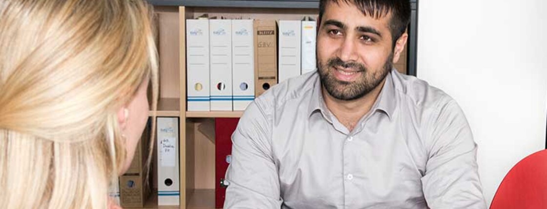 Beratungsgespräch in einem Büro: Zwei Personen besprechen Unterlagen und Formulare an einem Schreibtisch.