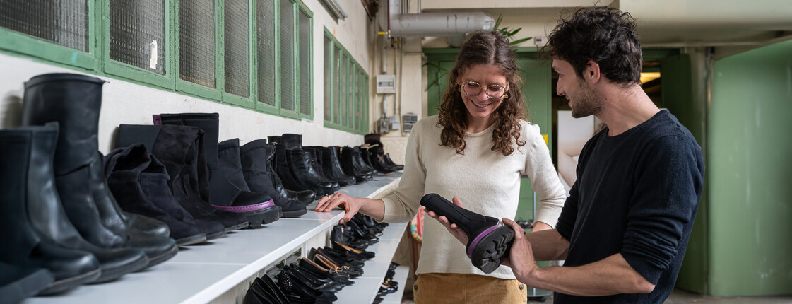 Second-Hand-Shopping und Beschäftigungsmöglichkeiten  Ein Mann und eine Frau stehen in einem Second-Hand-Shop vor Regalen mit schwarzen Schuhen und sortieren gemeinsam Schuhe aus.
