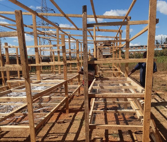 Innenansicht des Solartrockner-Aufbaus   Holzkonstruktion mit mehreren Trockengestellen, an der Personen arbeiten.