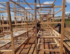 Innenansicht des Solartrockner-Aufbaus   Holzkonstruktion mit mehreren Trockengestellen, an der Personen arbeiten.