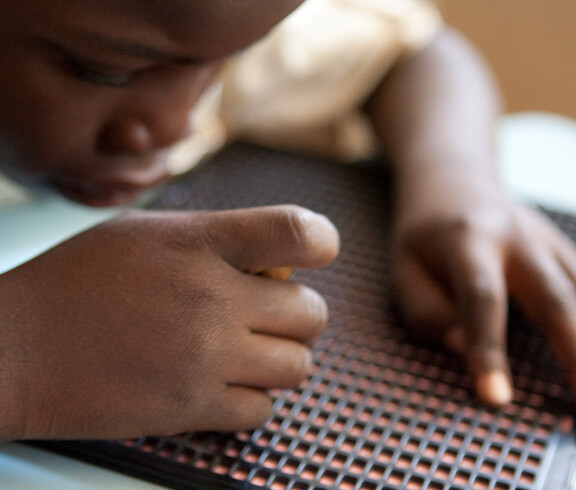 Blindes Kind liest mit den Händen auf einer Braille-Tafel