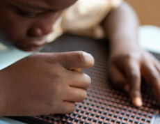 Blindes Kind liest mit den Händen auf einer Braille-Tafel