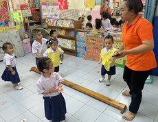 Mehrere Kinder und eine Lehrkraft bewegen sich spielerisch in einem bunten Klassenzimmer.