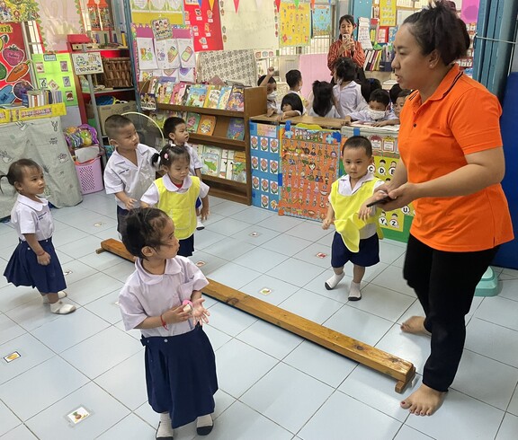 Mehrere Kinder und eine Lehrkraft bewegen sich spielerisch in einem bunten Klassenzimmer.