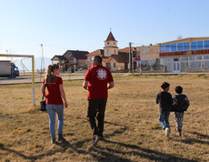 Caritas-Projektreferentin Theresa Sacher geht mit ihrem Caritas-Kollegen und Messie über einen Fußballplatz.