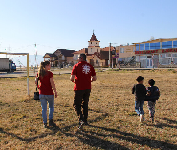 Caritas-Projektreferentin Theresa Sacher geht mit ihrem Caritas-Kollegen und Messie über einen Fußballplatz.