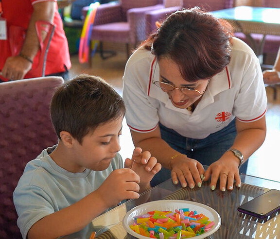 Betreuerin unterstützt ein Kind beim Spielen und Lernen mit bunten Stäbchen an einem Tisch