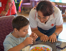 Betreuerin unterstützt ein Kind beim Spielen und Lernen mit bunten Stäbchen an einem Tisch