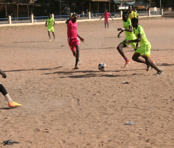 Zwei Spieler kämpfen während eines Fußballspiels auf Sandboden um den Ball.