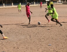 Zwei Spieler kämpfen während eines Fußballspiels auf Sandboden um den Ball.
