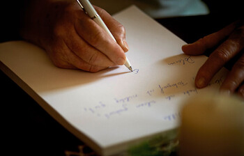 Eine Hand mit Kugelschreiber in der Hand schreibt etwas auf dein Blatt Papier.