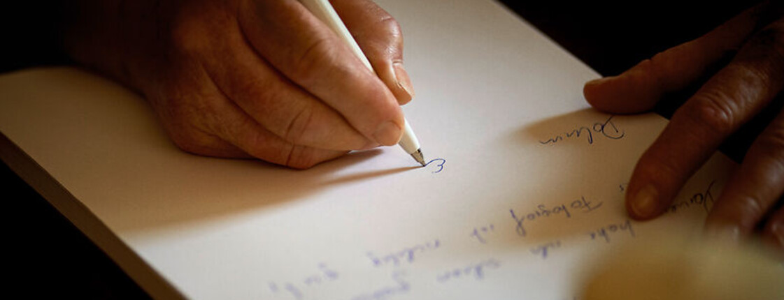 Eine Hand mit Kugelschreiber in der Hand schreibt etwas auf dein Blatt Papier.