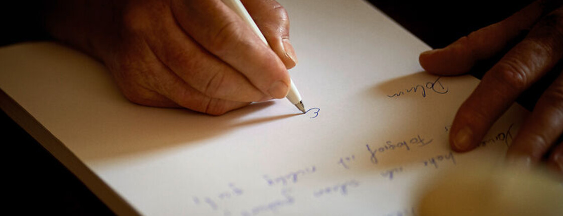 Eine Hand mit Kugelschreiber in der Hand schreibt etwas auf dein Blatt Papier.