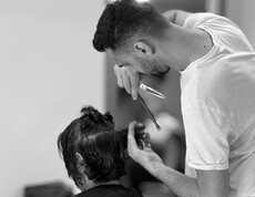 Eine Person schneidet einer sitzenden Person mit einer Schere die Haare