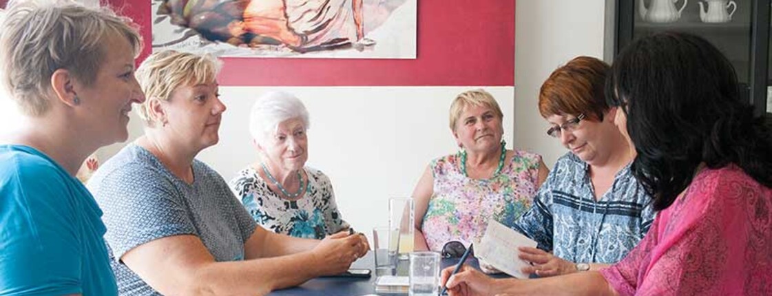 Mehrere Frauen sitzen gemeinsam an einem Tisch in einem Raum und unterhalten sich.