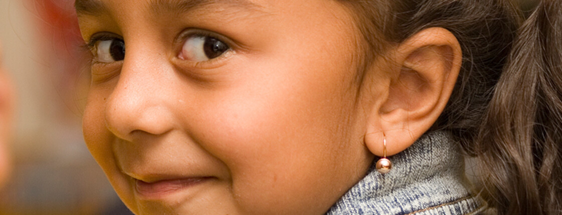Ein Mädchen mit Ohrring lächelt seitlich in die Kamera.
