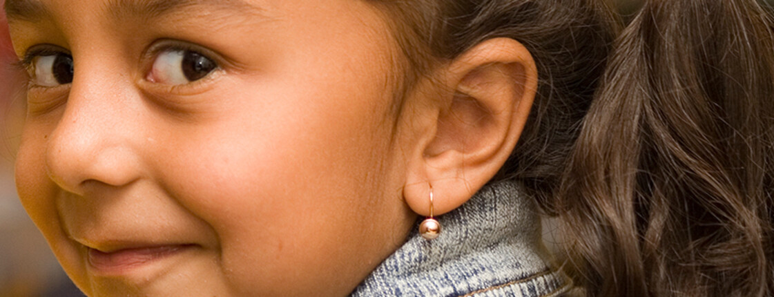 Ein Mädchen mit Ohrring lächelt seitlich in die Kamera.