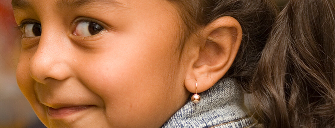 A girl with an earring smiles sideways at the camera.