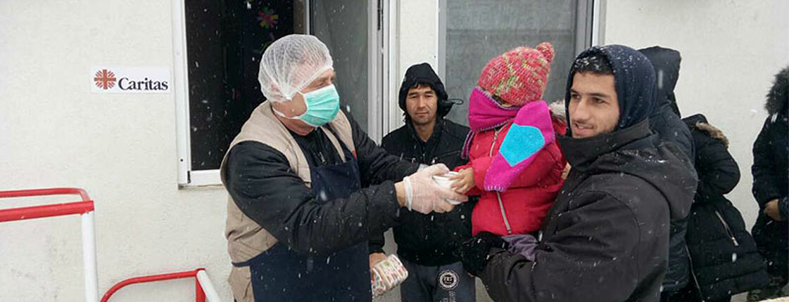 Ein Caritas Mitarbeiter gibt ein Lebensmittelpaket an einen Flüchtling und sein Kind.