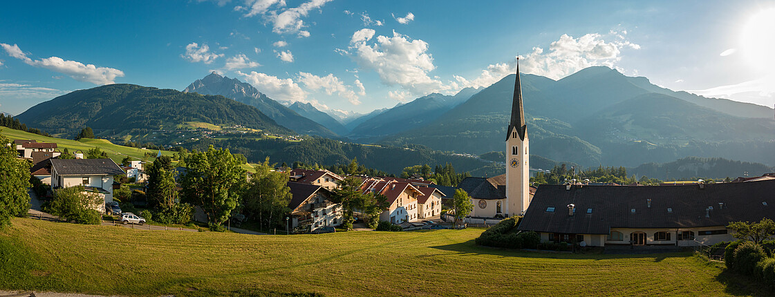 Panorama einer kleinen Gemeinde mit Kirchturm vor Tiroler Bergkulisse.